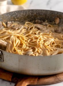 Creamy carbonara linguine with mushrooms in a large skillet with a wooden spoon.