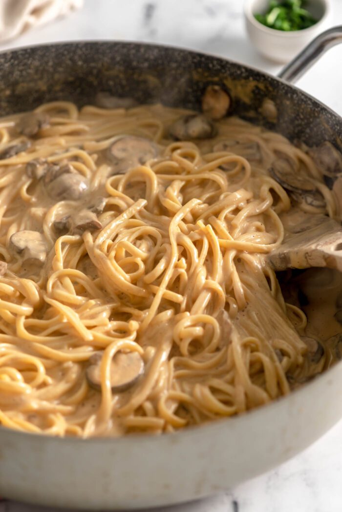 Creamy carbonara linguine with mushrooms in a large skillet with a wooden spoon.