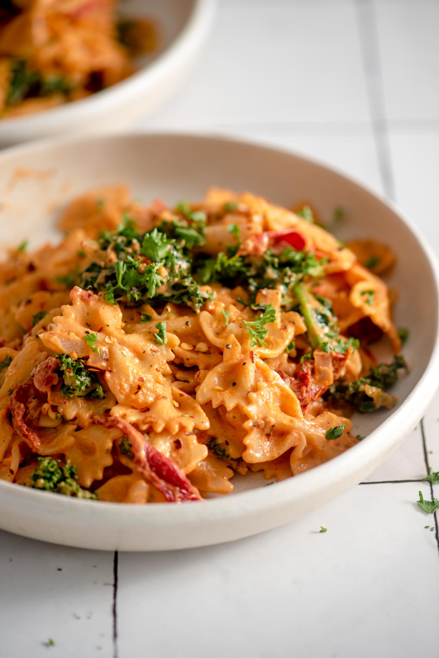 A bowl of sun dried tomato pasta with kale and fresh parsley on top.