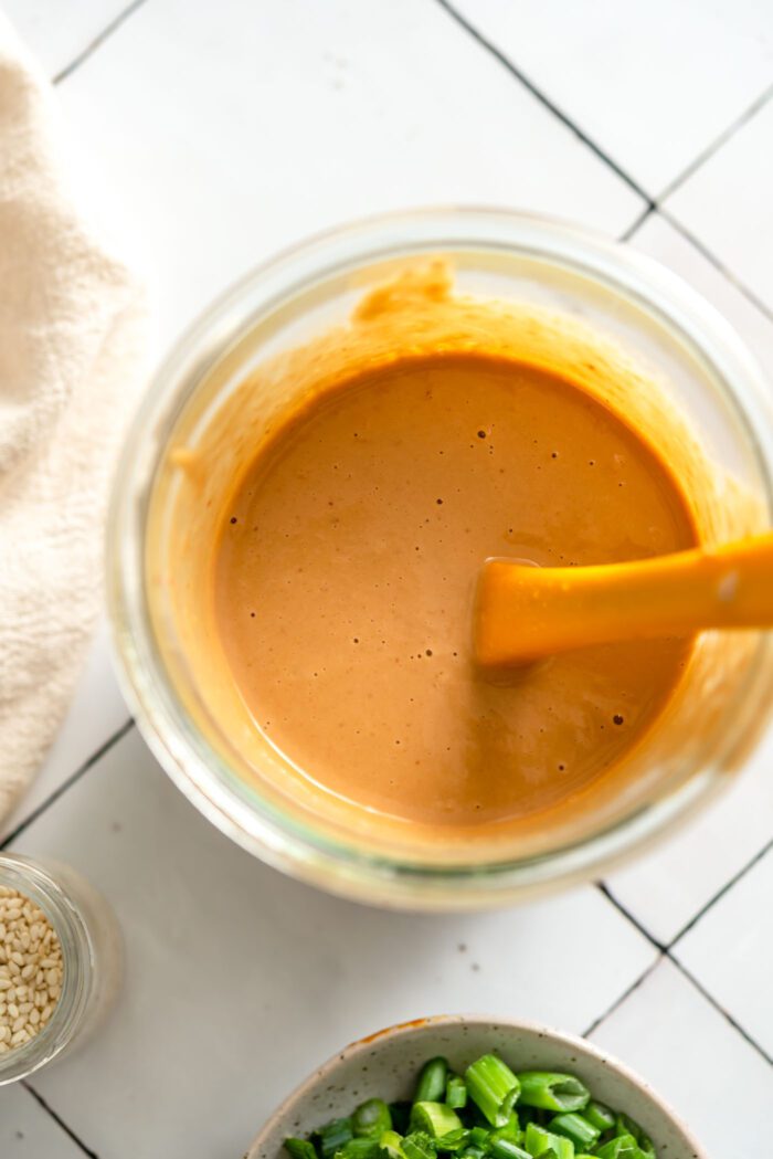 Creamy peanut sauce in a glass jar with a small spatula.