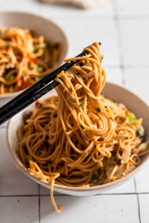 Chopsticks lifting noodles from a small bowl.