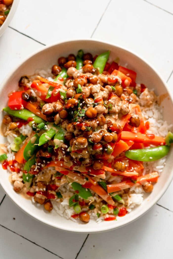 Overhead view of a rice bowl with stir fried carrot, snap pea and bell pepper and teriyaki chickpeas with green onion.