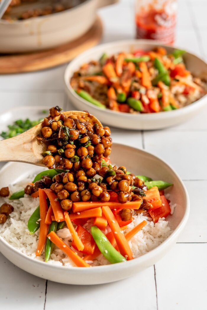 Scooping teriyaki chickpeas onto a bowl of rice and vegetables.