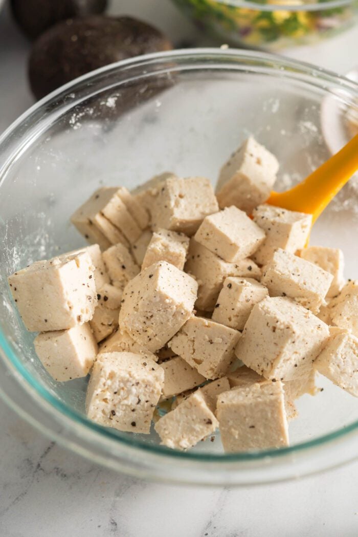 Cubed tofu in a bowl mixed with cornstarch, salt and pepper.