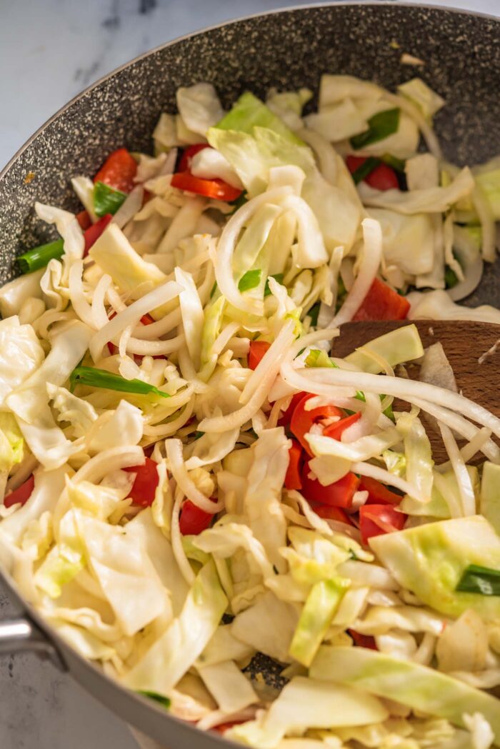 Cabbage, bell pepper, onion and green onion cooking in a large pan.