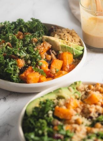 Two quinoa power bowls with butternut squash, chickpeas, kale and avocado. A jar of maple dijon dressing is in the background.