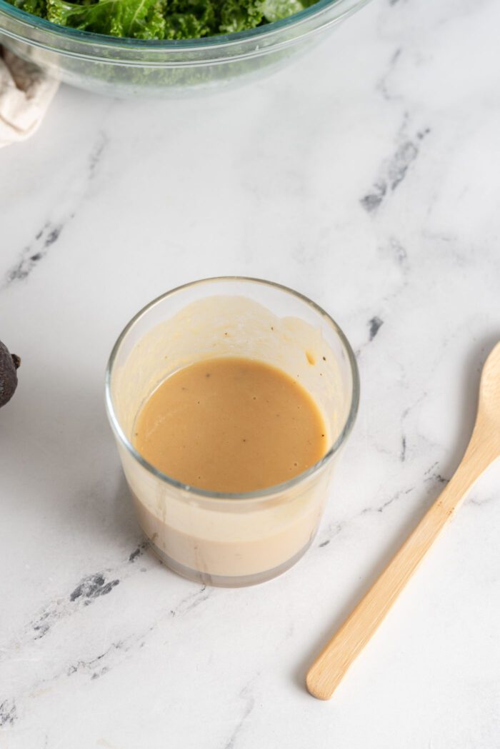 Small glass of creamy maple tahini dressing with a wooden spoon resting beside it.