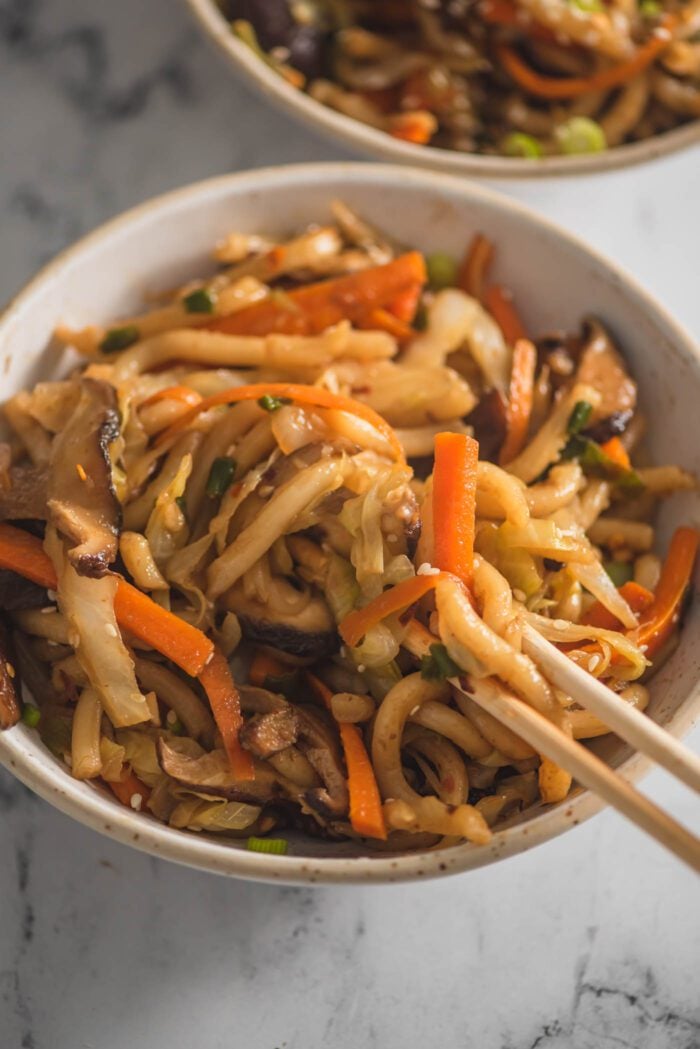 Chopsticks scooping yaki udon with vegetables from a bowl.
