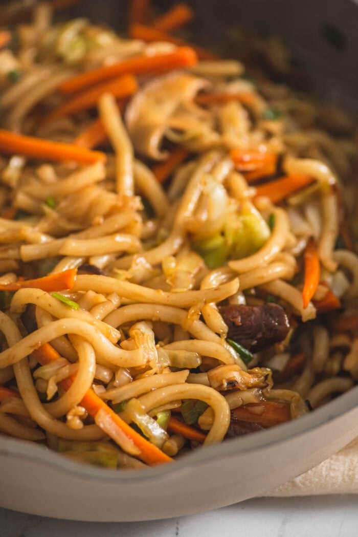 Close up of a udon noodle stir fry recipe with vegetables in a large wok.