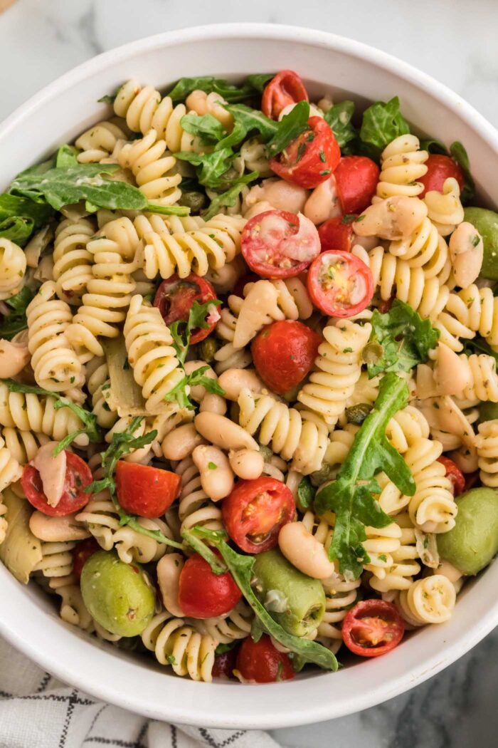 Overhead view of a zesty Italian pasta salad with rotini, greens, tomato, artichokes and fresh herbs.