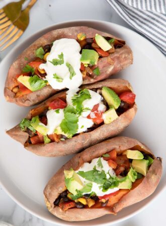 Overhead view of three sweet potatoes stuffed with black bean, corn and bell pepper and topped with sour cream, cilantro and avocado.