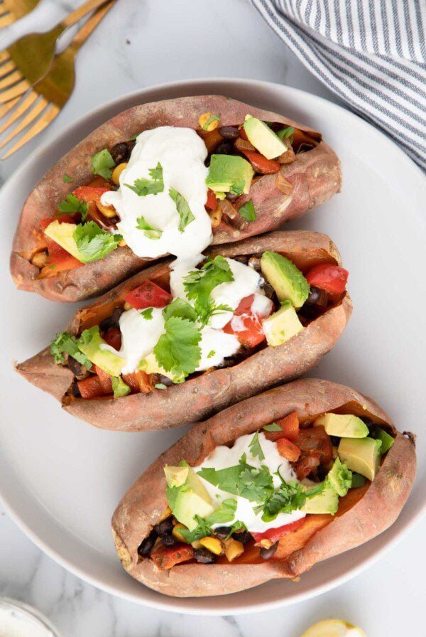 Overhead view of three sweet potatoes stuffed with black bean, corn and bell pepper and topped with sour cream, cilantro and avocado.