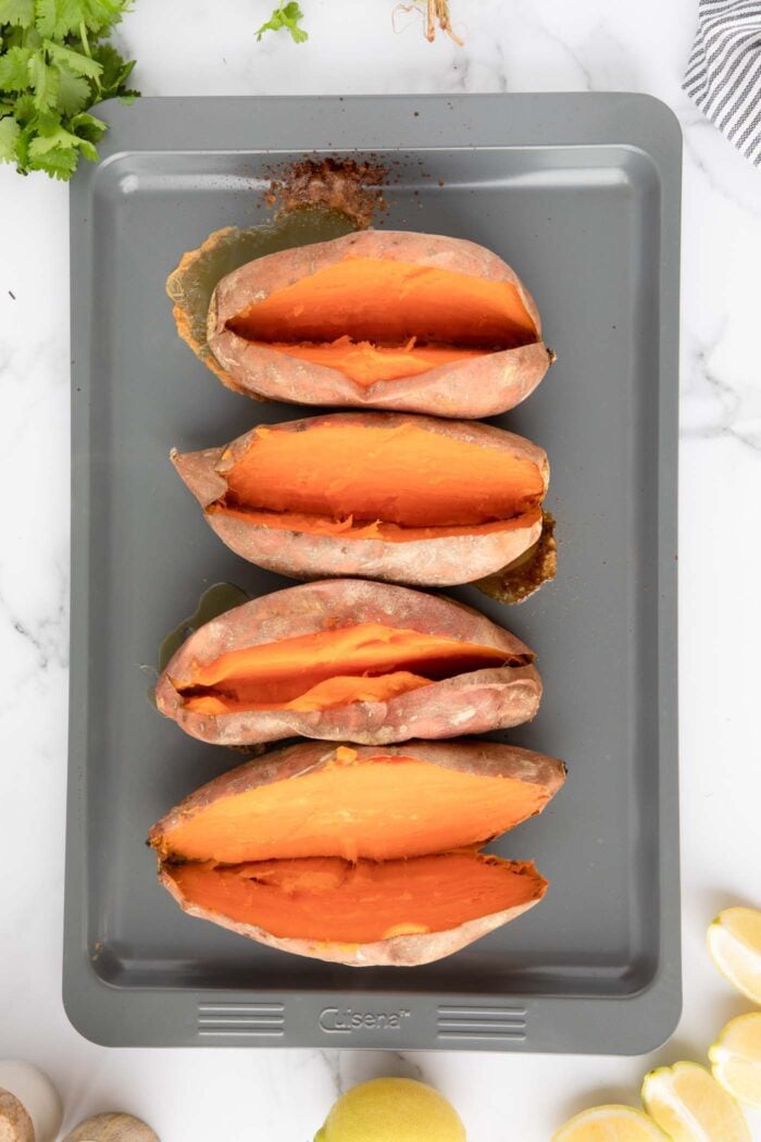 4 baked sweet potatoes sliced open lengthways on a baking tray.