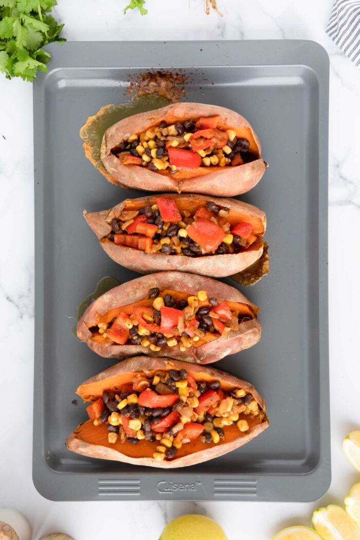 4 baked sweet potatoes stuffed with a black bean, corn and bell pepper filing on a baking tray.