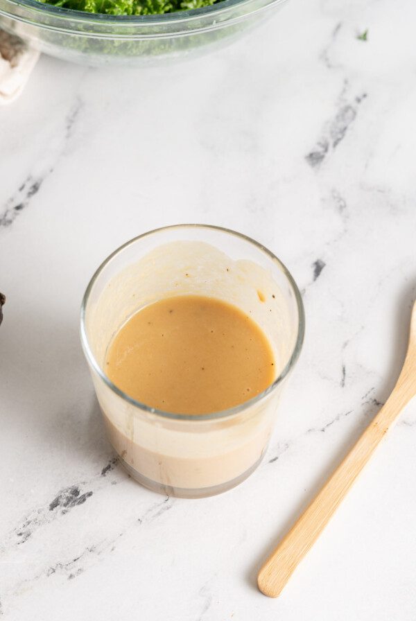 Overhead view of a jar of creamy maple tahini dijon dressing with a small wooden spoon resting beside it.