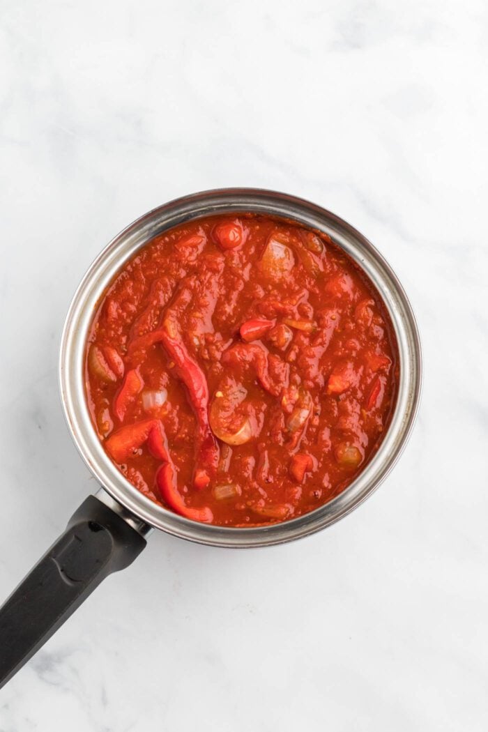 Red tomato sauce with onion and bell pepper cooking in a saucepan.
