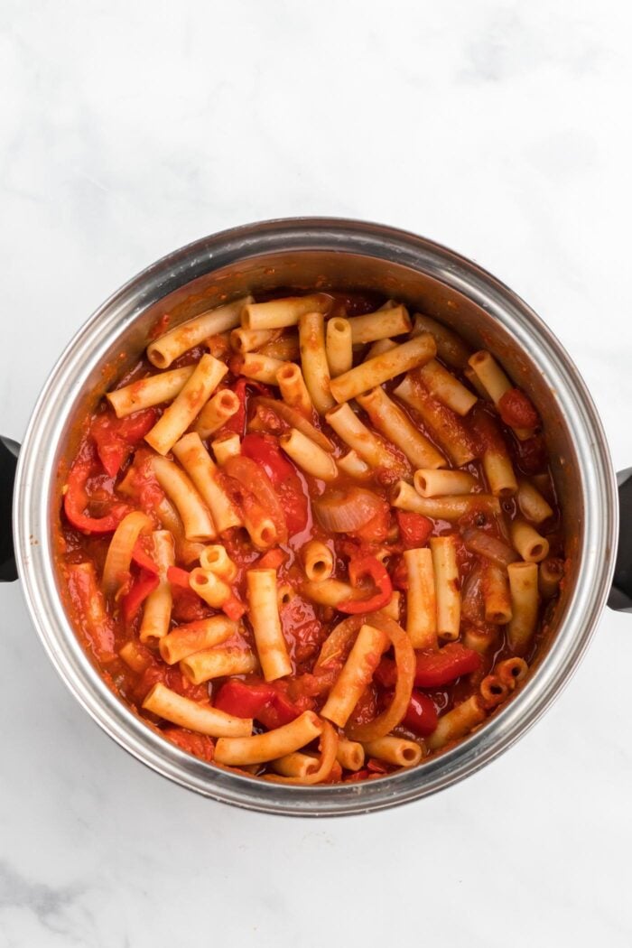 Ziti pasta mixed with tomato sauce, onion and bell pepper in a saucepan.