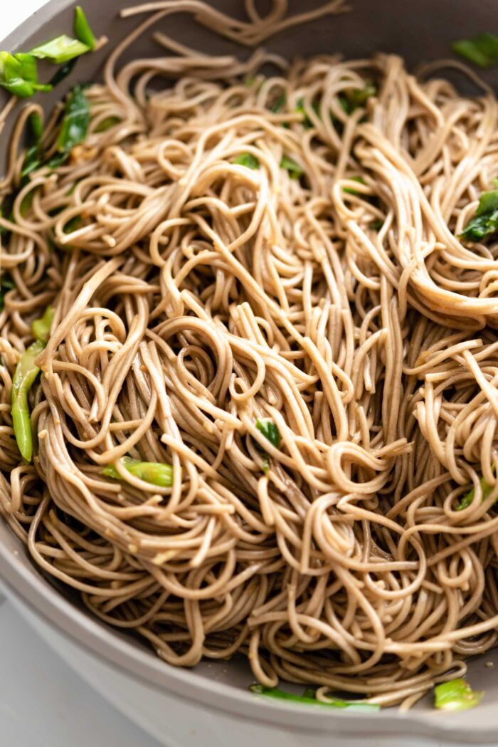 Soba noodles in sesame garlic sauce with green onions cooking in a pan.