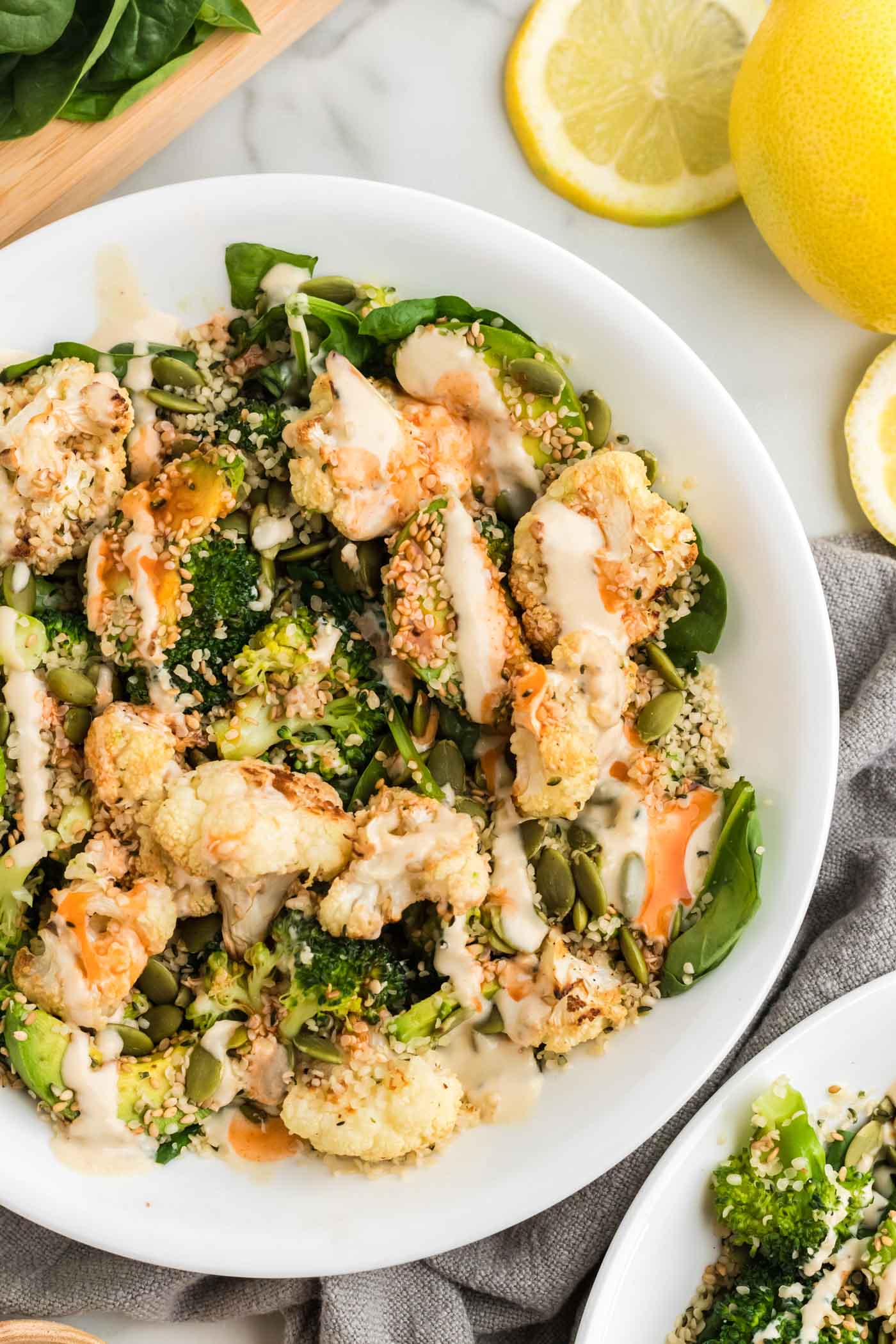 Healthy broccoli and cauliflower salad with avocado, hemp seeds and sesame seeds and topped with tahini sauce and hot sauce in a bowl.