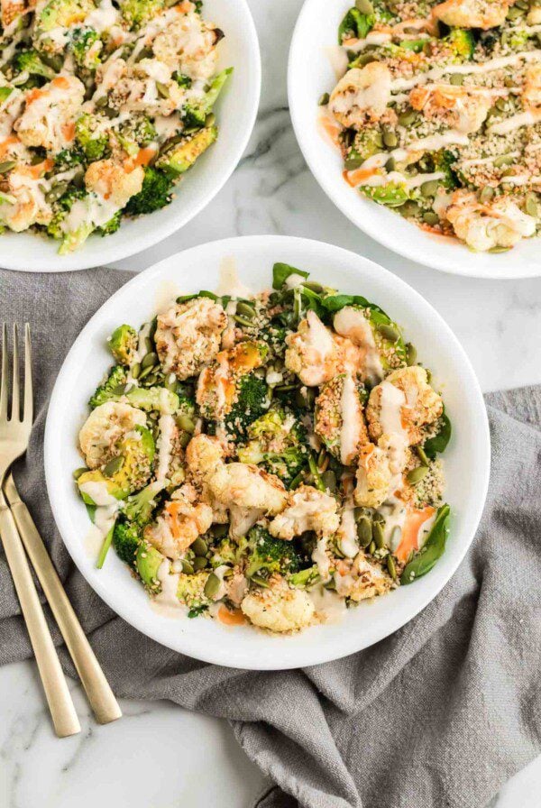 Healthy broccoli and cauliflower salad with avocado, hemp seeds and sesame seeds and topped with tahini sauce and hot sauce in a bowl.