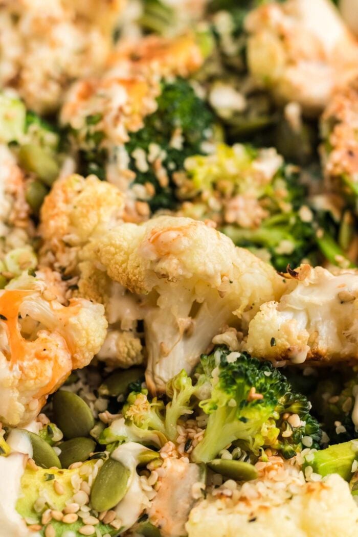 Close up of a roasted cauliflower and broccoli salad with spinach, tahini dressing, seeds and hot sauce.