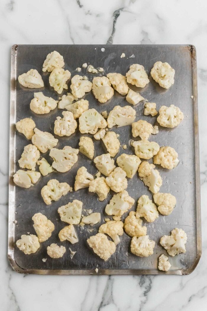 Cauliflower florets tossed with oil, salt and pepper on a roasting pan.