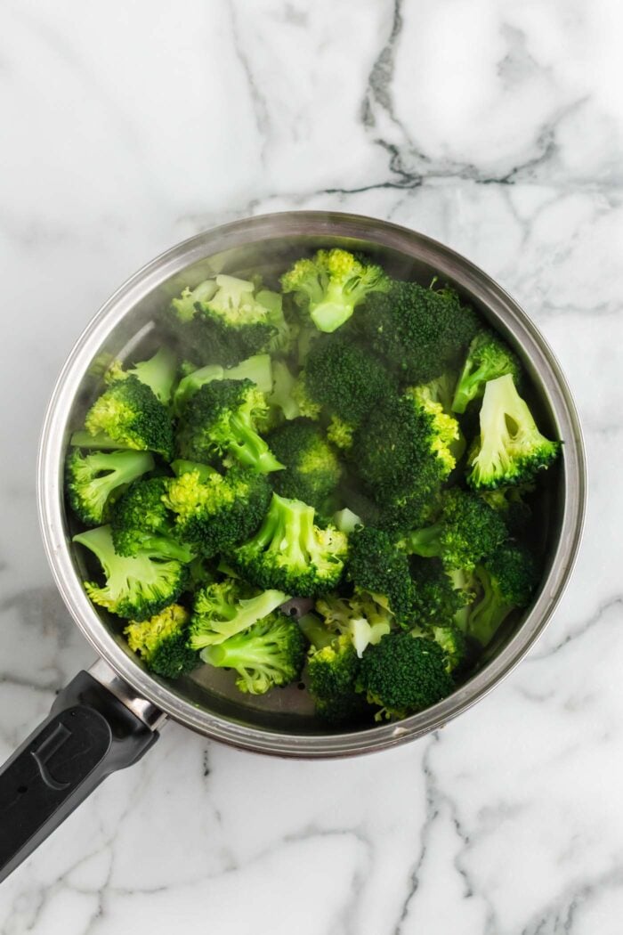 Steaming pot of freshly steamed broccoli florets on a marble surface.