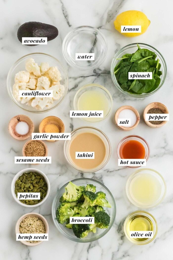 All the ingredients needed for making a healthy broccoli and cauliflower salad with seeds, spinach and avocado. Each ingredient is labelled with text describing the ingredient.