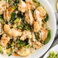 Healthy broccoli and cauliflower salad with avocado, hemp seeds and sesame seeds and topped with tahini sauce and hot sauce in a bowl.