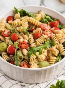 Large bowl of zesty Italian pasta salad with artichokes, olives, tomato and arugula.