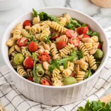 Large bowl of zesty Italian pasta salad with artichokes, olives, tomato and arugula.