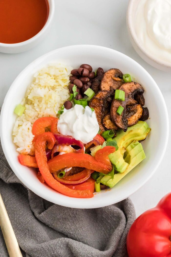 Vegetarian fajita bowls with cooked bell peppers and onions, avocado, rice, sour cream, black beans and marinated cooked mushrooms.