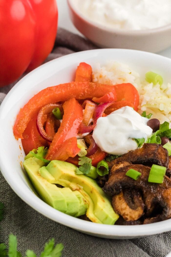 Close up of a vegetarian veggie fajita bowl with sour cream, peppers and onions, avocado, black beans and rice.
