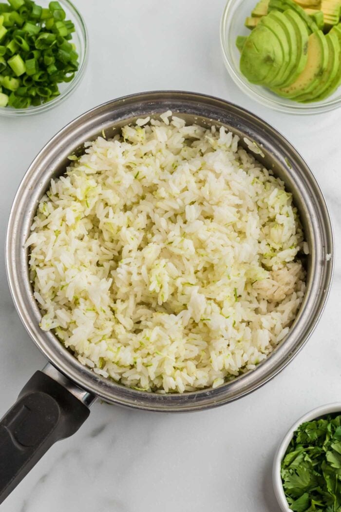 Cooked rice with lime zest and cumin in a sauce pan.