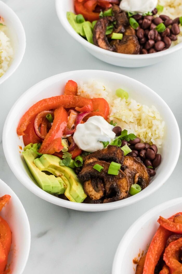 Vegetarian fajita bowls with cooked bell peppers and onions, avocado, rice, sour cream, black beans and marinated cooked mushrooms.
