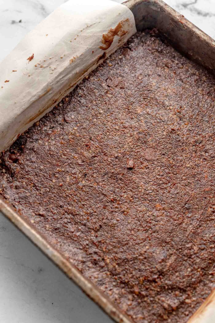 No-bake chocolate brownies pressed into a square baking pan lined with parchment paper.