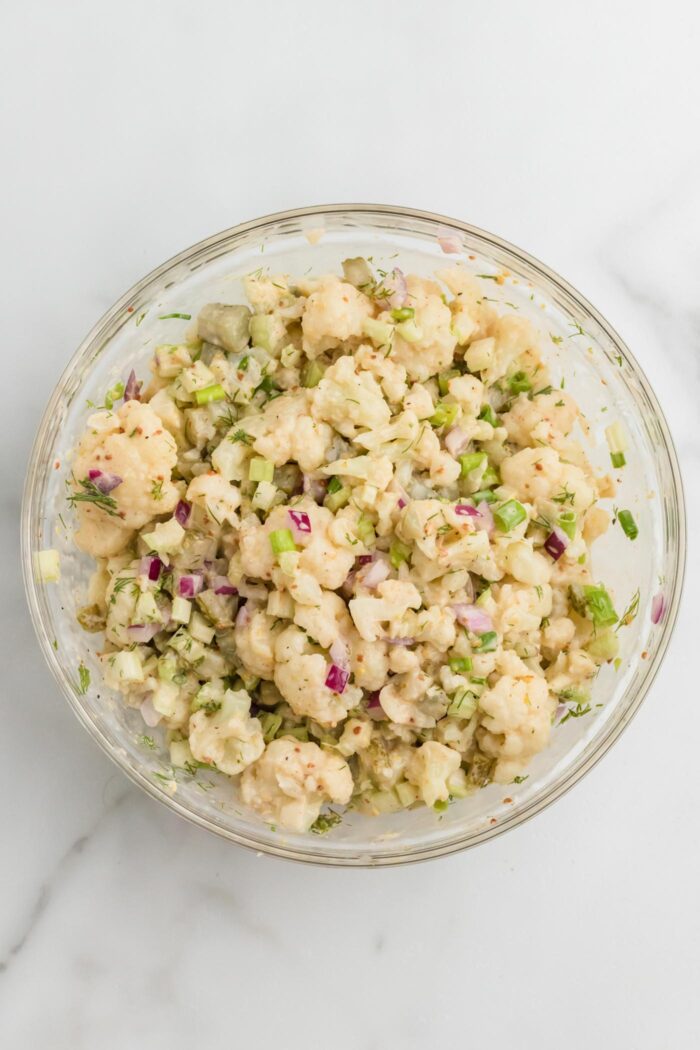 No potato "potato" salad made with cauliflower mixed up in a glass mixing bowl.