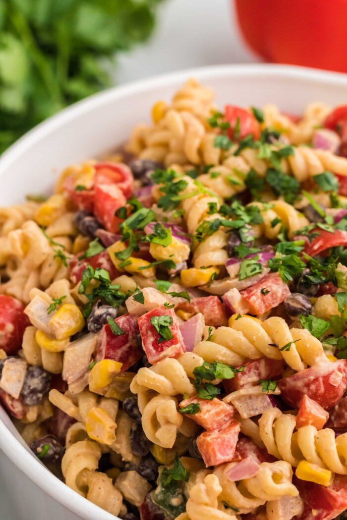 Close up of a mixing bowl of creamy Southwestern pasta salad with bell pepper, corn, onion, jalapeno, black beans, tomato and cilantro.