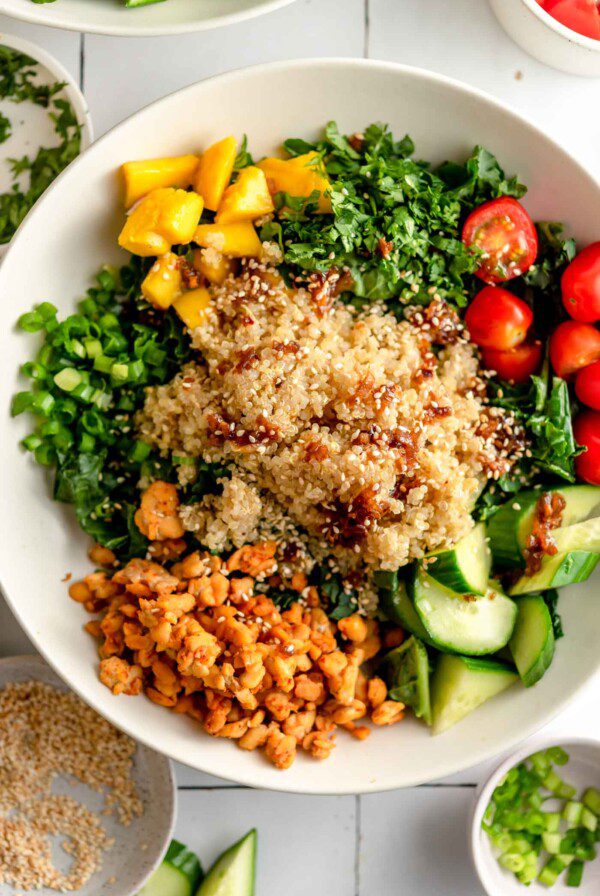 Overhead view of a colourful quinoa grain bowl with avocado, mango, tempeh, cucumber, cilantro, tomato and green onion.