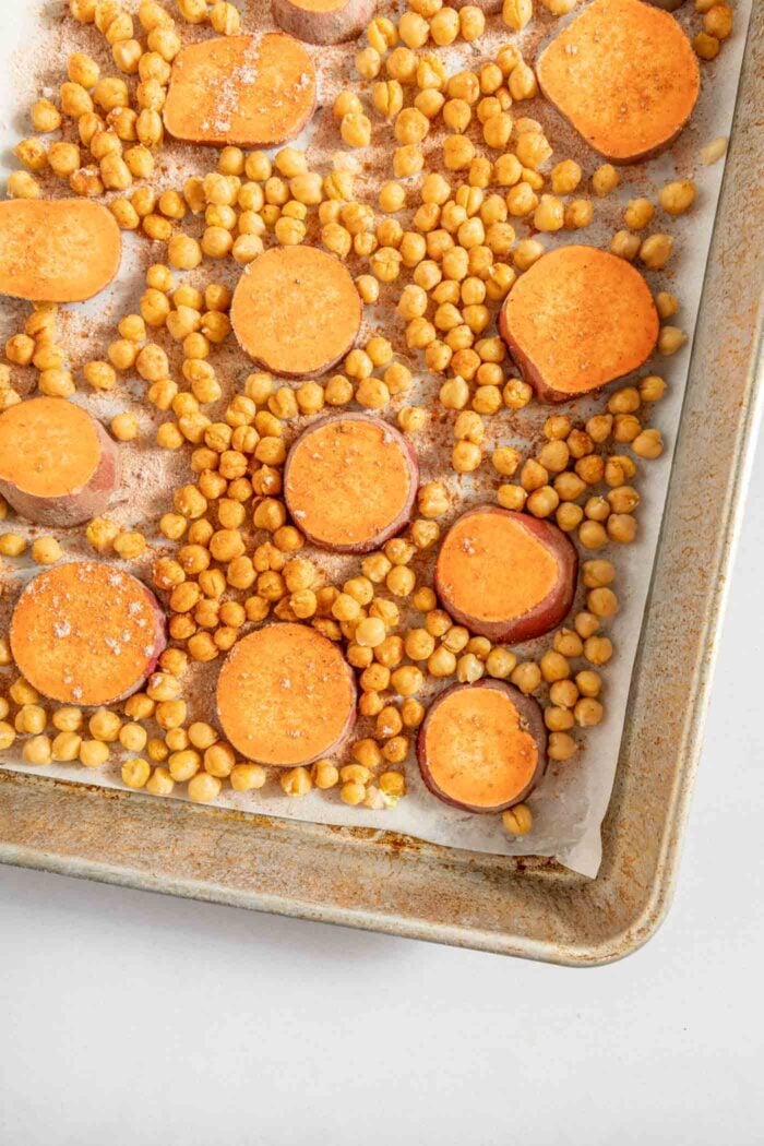 Sweet potato rounds and chickpeas on a baking tray spinkled with salt, pepper and spices.