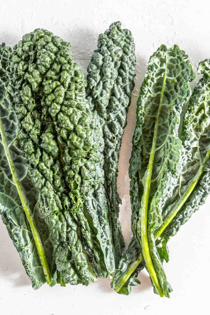 A number of leaves of lacinato, or Tuscan kale on a white surface.