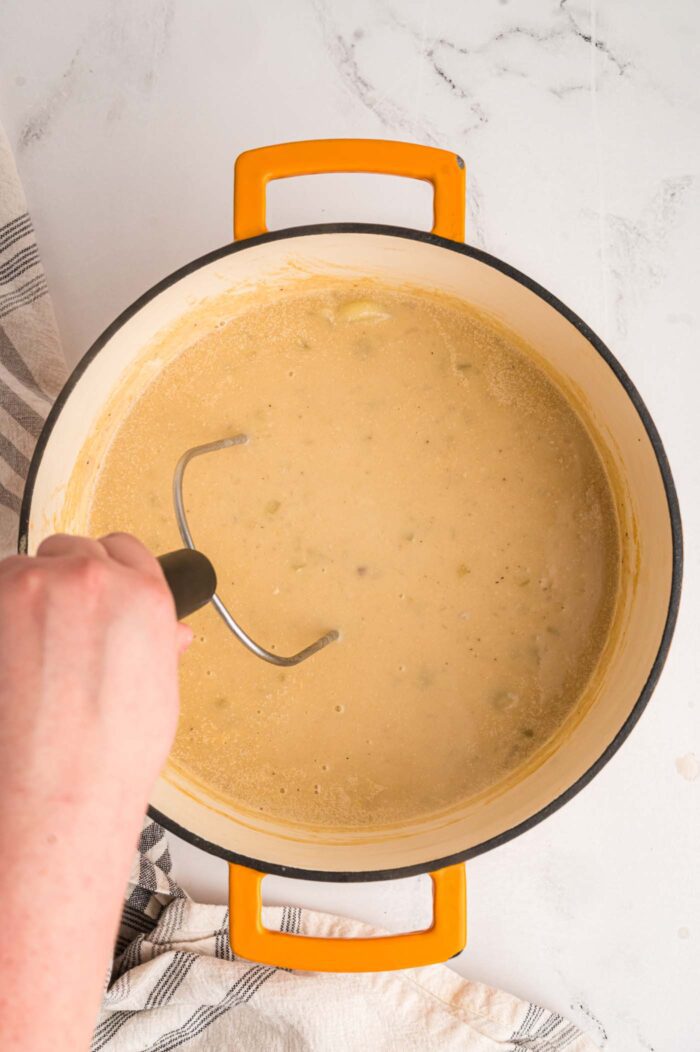 Using a potato masher in a large soup pot of creamy potato soup.