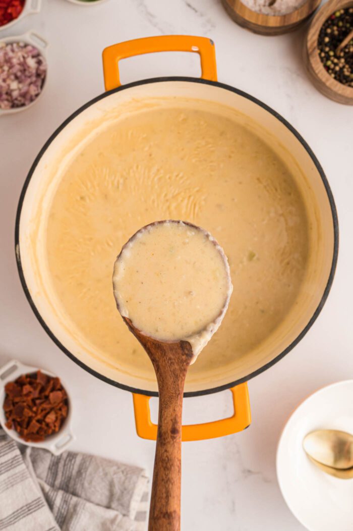 Wooden spoonful of creamy potato soup held over a pot of potato soup.