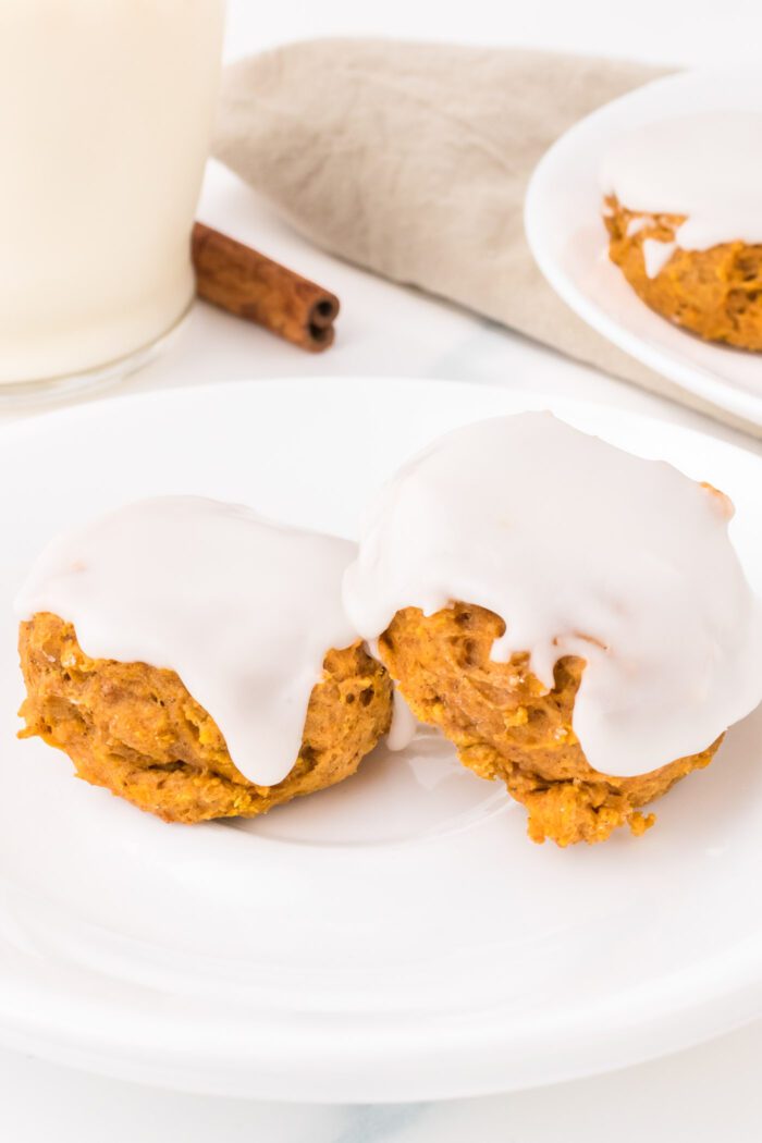 Two soft pumpkin cookies topped with icing on a small plate.