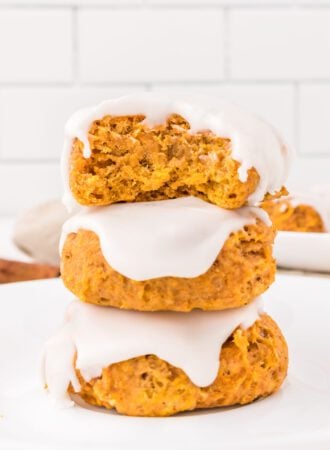 Stack of 3 soft pumpkin cookies topped with icing. The cookie on top has a bite out of it so you can see the texture inside.