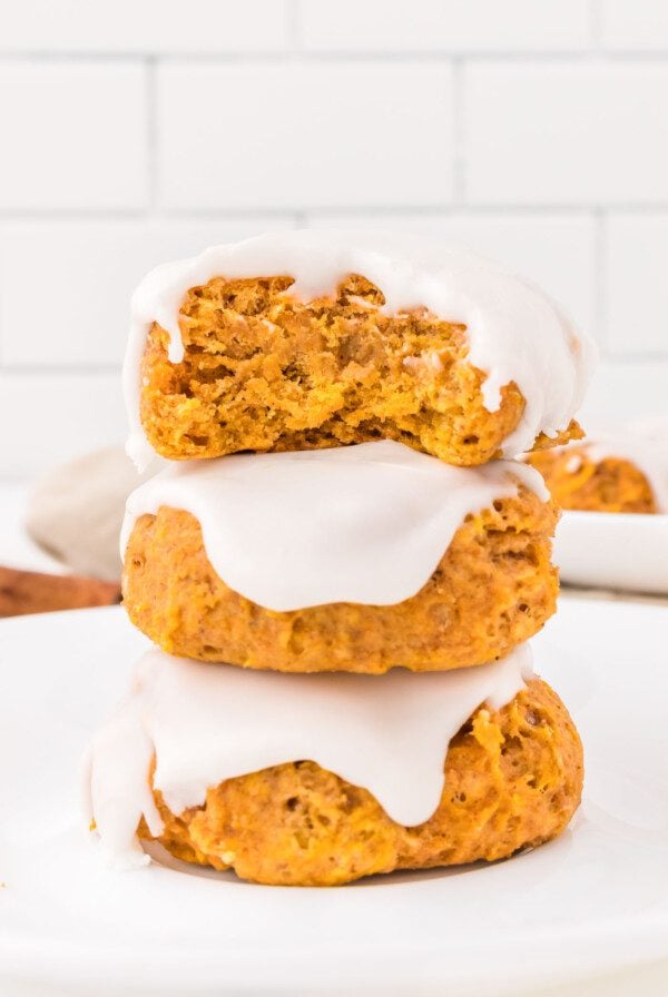 Stack of 3 soft pumpkin cookies topped with icing. The cookie on top has a bite out of it so you can see the texture inside.