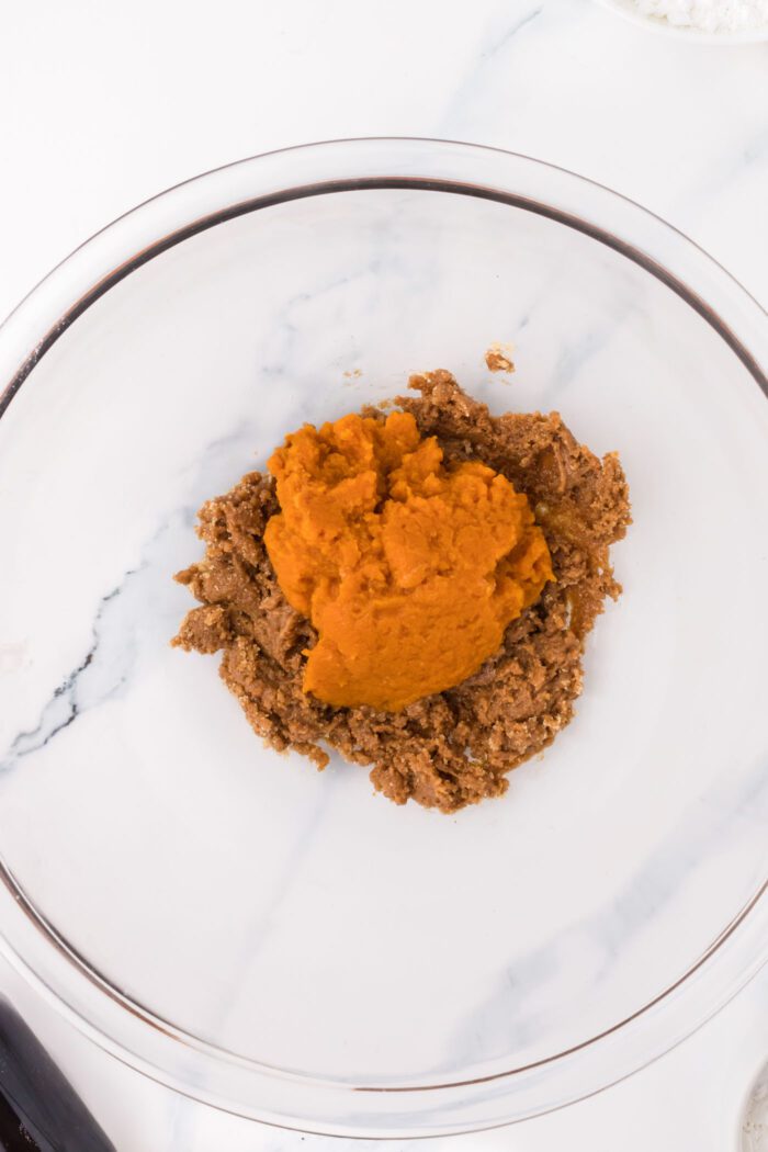 Almond butter mixed with brown sugar in a glass mixing bowl with a scoop of pumpkin puree on top.