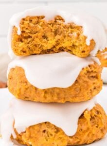 Stack of 3 soft pumpkin cookies topped with icing. The cookie on top has a bite out of it so you can see the texture inside.