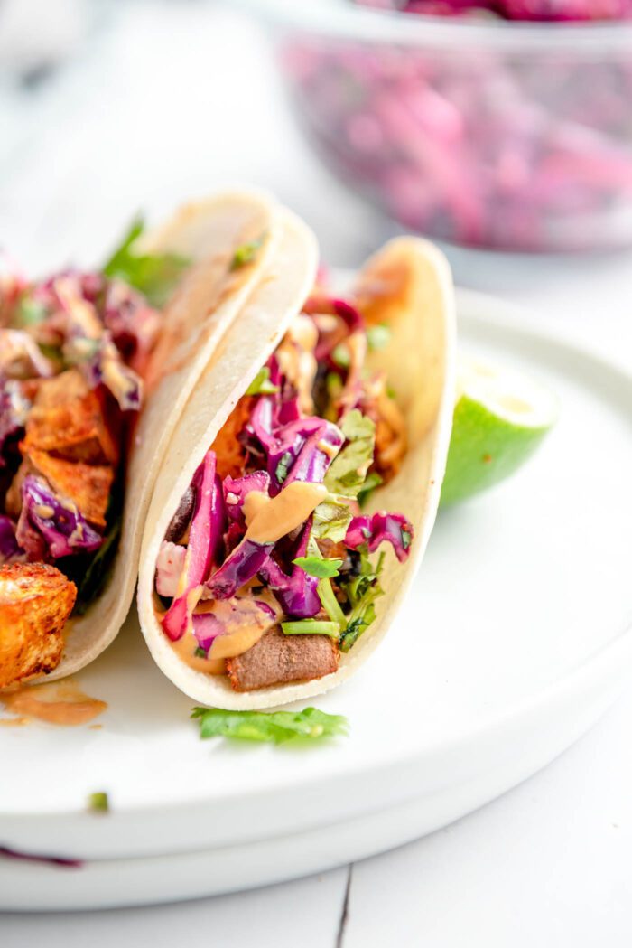 Two folded over black bean and sweet potato tacos with red cabbage slaw and queso sauce on a plate. 