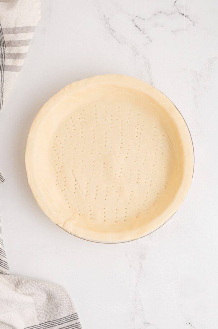An unbaked pie crust perforated with small holes from a fork in a pie dish.